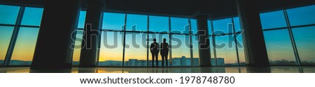The two men stand on the panoramic window background