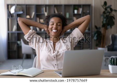 Happy millennial generation african ethnicity woman resting on chair with folded arms behind head and closed eyes, feeling relaxed on after finishing difficult online project on computer in office. Royalty-Free Stock Photo #1978757669