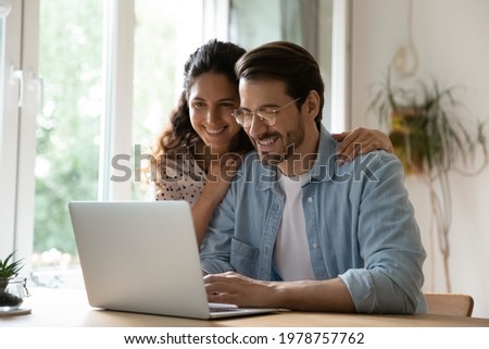 Smiling sincere married couple web surfing information online, using computer software application, enjoying planning summer vacation together, booking flight tickets or hotel, shopping in internet.