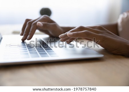 Close up young mixed race african woman typing on keyboard on laptop, working on online project in corporate software application, web surfing information online, texting email communicating distantly Royalty-Free Stock Photo #1978757840