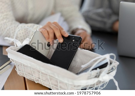 Close up cropped of young woman employee businesswoman putting phone in basket, involed in meeting with colleague, free from smartphone, no cellphone zone in office or digital detox concept Royalty-Free Stock Photo #1978757906