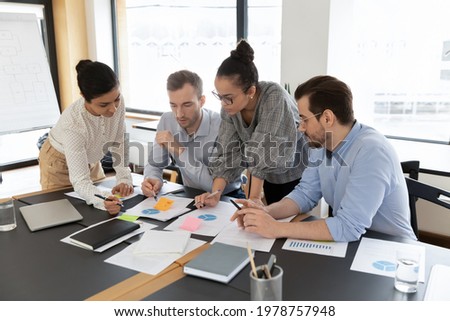 Diverse employees team coworkers discussing project strategy, working with documents, analyzing financial statistics, developing strategy, brainstorming in boardroom, teamwork and cooperation