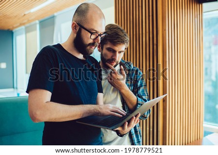 Caucaisan male colleagues browsing web information and publication in social networks using wireless connection in coworking space, skilled hipster guys making online booking and banking via app
