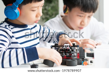Science, Technology, Engineering and Mathematics (STEM) education concept. Two smart looking Asian young kids with headphone assemble and test a robot with EV3 components as school project at home. Royalty-Free Stock Photo #1978789907