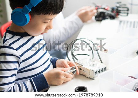 Science, Technology, Engineering and Mathematics (STEM) education concept. Two smart looking Asian young kids with headphone assemble and test a robot with EV3 components as school project at home. Royalty-Free Stock Photo #1978789910