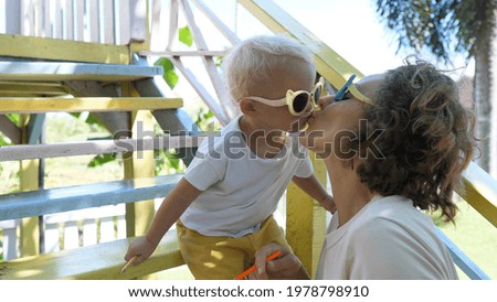 Young Caucasian mother gives a kiss to her 2 years old baby daughter on a playground