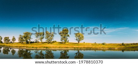 Panorama Of Blue Night Starry Sky Above Lake River. Night Glowing Stars And Trees Woods Reflected In Water. Beautiful Night Landscape With Natural Glowing Stars