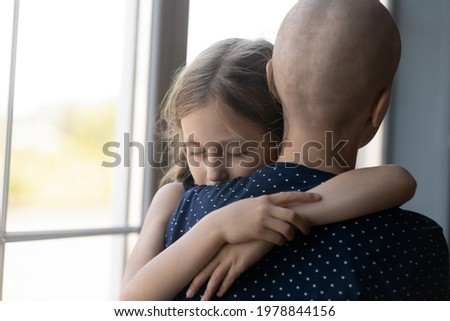 Sad serious daughter girl with closed eyes hugging hairless mom with cancer. Pre teen child giving comfort and support to mother fighting against oncological disease. Oncology, family concept Royalty-Free Stock Photo #1978844156