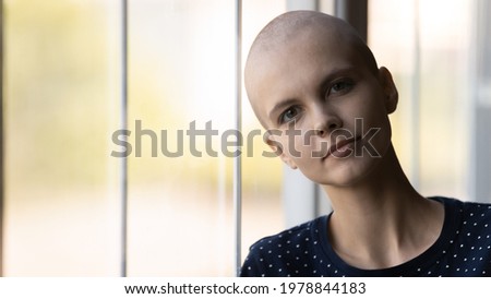 Portrait of serious cancer patient fighting against oncological disease, going through treatment, chemotherapy, hoping for recovery. Hairless woman standing by window, looking at camera. Head shot