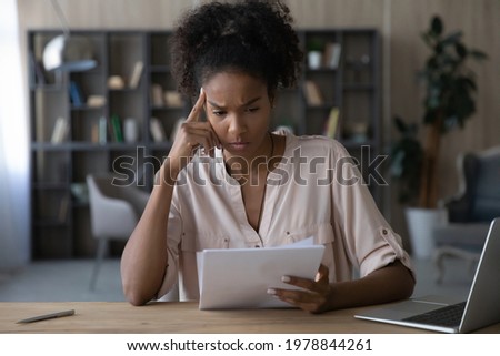 Unhappy young african american woman looking through paper document, reading unpleasant news or research report with bad results. Frustrated mixed race brazilian lady getting bank loan rejection. Royalty-Free Stock Photo #1978844261