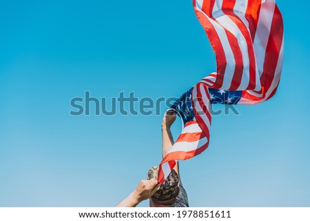 Man in military uniform holding american flag over clear sky