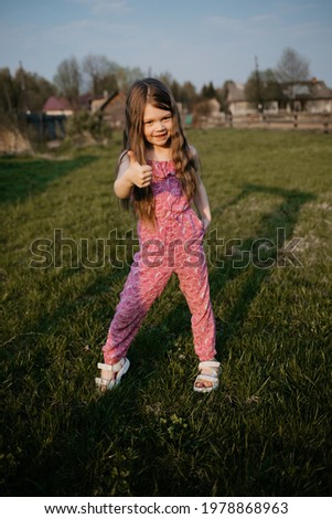 A girl with long hair in summer stands on the lawn in the village under the setting sun. image with selective focus and noise effect 