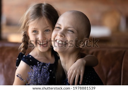 Portrait of happy overjoyed mom with cancer and little daughter celebrating mothers day, birthday, holiday, holding bunch of flowers, having fun, hugging, smiling, laughing, looking away. Hope concept
