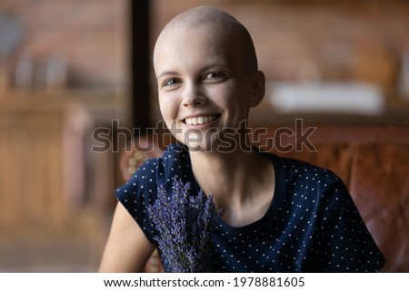 Portrait of happy young hairless woman getting good result of treatment and chemotherapy, celebrating beating cancer, holding bouquet of fresh field flowers, looking at camera, smiling. Head shot