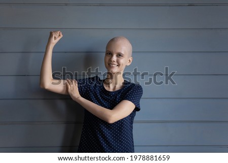 Happy strong cancer patient winning battle for life, getting better. Hairless optimistic woman showing hand muscles and fist, expressing strength and joy for successful treatment. Head shot portrait