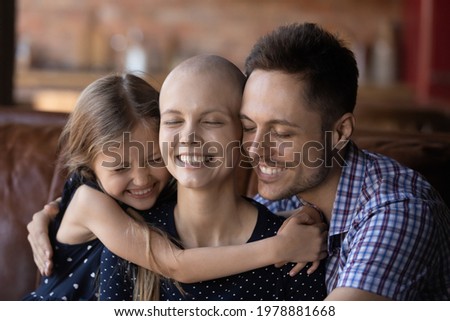 Happy daughter kid and dad hugging ill hairless mom, fighting against cancer. Young couple and child sitting together on couch, embracing with closed eyes. Oncology concept. Headshot portrait