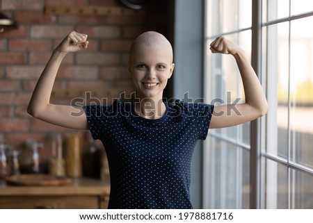 Happy strong female cancer patient flexing hands, biceps and fists, showing strength and confidence in fighting against disease. Woman successfully struggling and beating oncology. Headshot portrait.