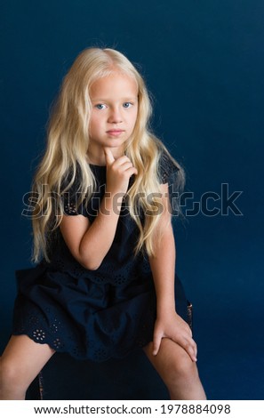 beautiful blonde in a dark blue dress on a solid blue background. The photo is great for demonstrating the character of a child - daydreaming, enthusiasm, vulnerability, touching, beauty, stubbornness