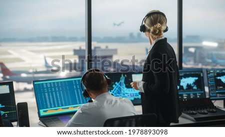 Female and Male Air Traffic Controllers with Headsets Talk in Airport Tower. Office Room is Full of Desktop Computer Displays with Navigation Screens, Airplane Departure and Arrival Data for the Team. Royalty-Free Stock Photo #1978893098