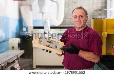 Elderly worker checks metal detail on a wooden sample. High quality photo