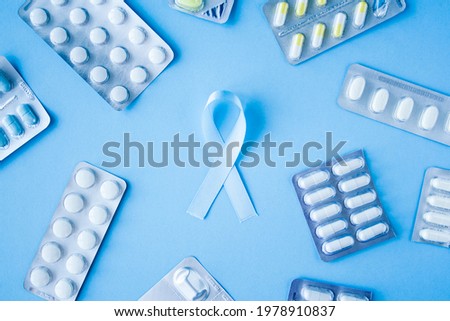 Blue ribbon symbol of prostate cancer with many pills and drugs clusters on bright background. Cancer awareness, cure, treatment concept. Oncology and carcinoma, ribbon