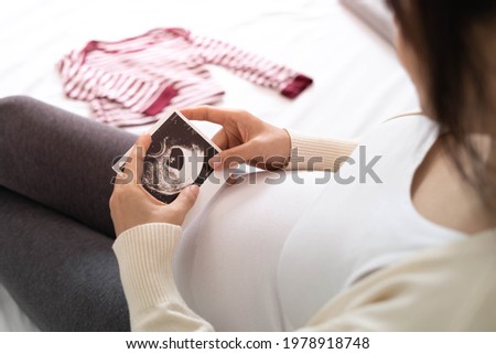The pregnant woman is happy to look at the baby ultrasound pictures and prepare some clothes for her.