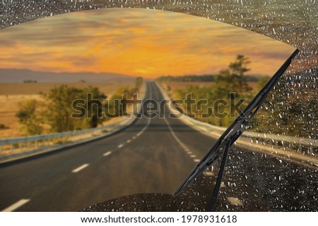 Car windshield wiper cleaning water drops from glass while driving Royalty-Free Stock Photo #1978931618