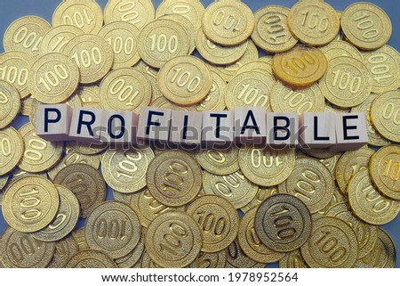 Profitable text on wood block with a pile of gold coins