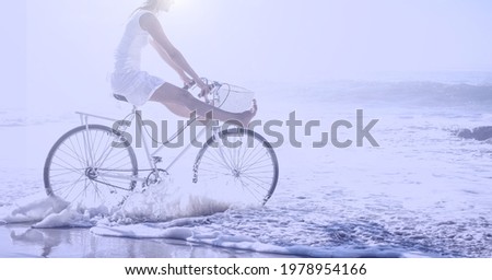 Composition of woman riding bike on beach with copy space. holiday, sport, fitness and active lifestyle concept digitally generated image.