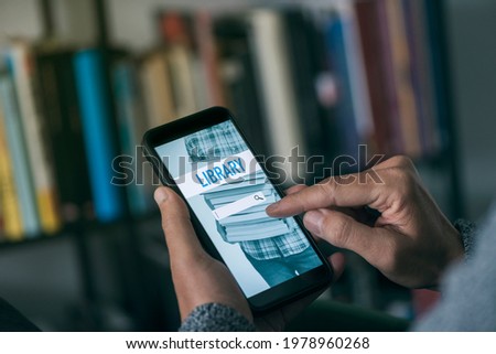 closeup of a young caucasian man, at home, searching an ebook to lend on an online library with his smartphone, with a simulated search engine in its screen