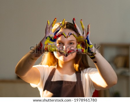 Love painting. Female artist. Creative lifestyle. Art studio. Inspiration muse. Happy artistic woman in apron showing heart sign hands with colorful paints light room interior.