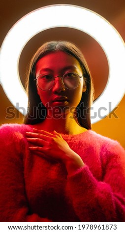Neon light people. Cyberpunk portrait. Futuristic beauty. Asian girl in glasses with LED round halo in pink yellow glow isolated on golden color gradient background.