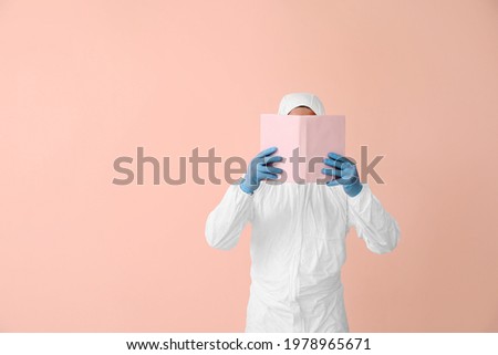Man in biohazard suit reading book on color background