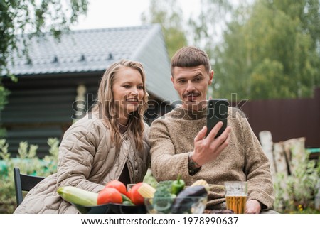Selfies on a smartphone for social networks are made by a girl and a guy sitting at a picnic table in the fresh air in the countryside.