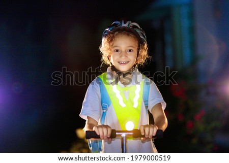 Kid in reflective vest in darkness. Safety on dark city streets for school children. Safe way home at night or in the evening. Fluorescent stripes on kids clothing and backpack. Boy walking at dusk. Royalty-Free Stock Photo #1979000519