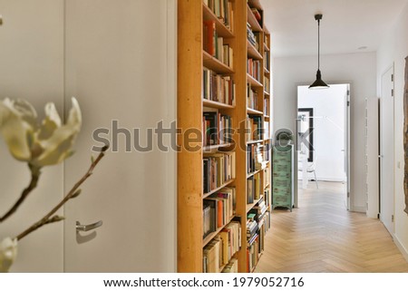 Perspective view of white apartment corridor with parquet floor and wooden bookcases with books under glowing lamps Royalty-Free Stock Photo #1979052716