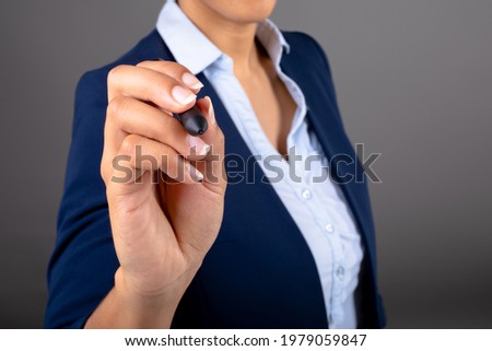 Mid section of african american businesswoman writing on invisible screen against grey background. business, professionalism and technology concept