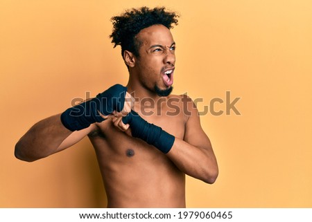 Young african american man with beard wearing boxing protection angry and mad screaming frustrated and furious, shouting with anger. rage and aggressive concept. 