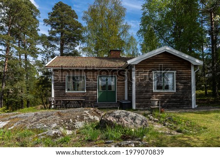 Old authentic cabin house in the woods. Dacha guest house. Nobody there. Old wooden building among forest trees for tourists relax. Roof tiles. Outdoors wooden table and chairs on the yard. Cozy place Royalty-Free Stock Photo #1979070839