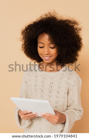 african american preteen girl looking at digital tablet in hands isolated on beige