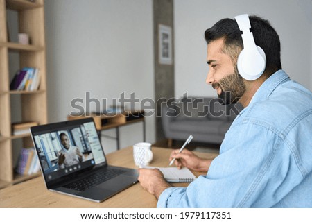 Latin indian adult student wearing headset having virtual meeting online call training educational webinar chatting with teacher at home office writing notes. Video e learning conference call on pc. Royalty-Free Stock Photo #1979117351