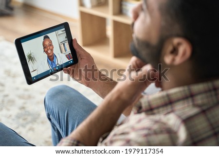 Young indian latin bearded businessman having videocall meeting at home with black female doctor therapist using tablet computer pointing to throat. Online virtual telemedicine health care concept. Royalty-Free Stock Photo #1979117354