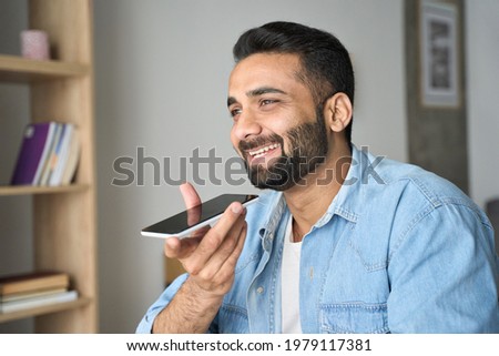 Young adult indian Hispanic handsome smiling man talking to voice assistant using cellphone smart phone gadget. Artificial intelligence and virtual reality technologies concept.
