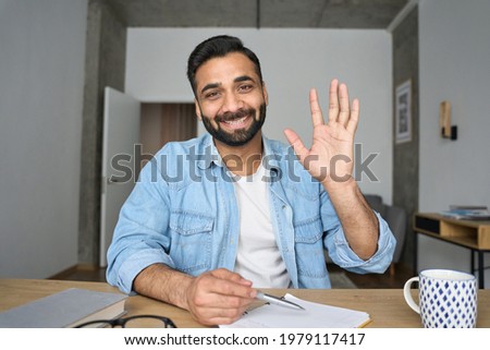 Young happy indian Hispanic arab teacher talking on video conference call greeting waving hand using laptop at modern home office. Remote distant online work education techs concept. Webcam view. Royalty-Free Stock Photo #1979117417