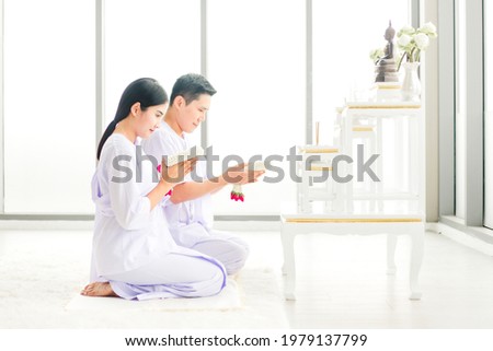 Buddhist couple wearing Thai traditional white dress holding jasmine garland for praying to buddha statue. Asian man and woman worship and meditation on Holy day. Royalty-Free Stock Photo #1979137799
