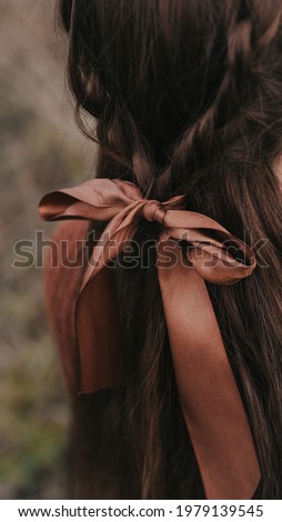 A brunette girl, as if from a book, stands with her back tied with a ribbon in her hair. Atmospheric frame