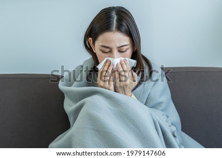 Sick, Coronavirus covid-19 asian young woman, girl headache under blanket have a fever, flu and use tissues paper sneezing nose, runny sitting on sofa bed at home. Health care on virus person. Royalty-Free Stock Photo #1979147606