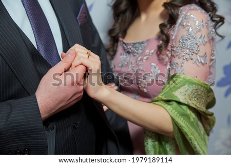 Newlyweds hold hands, showing wedding rings, against the background of autumn nature. Wedding portrait and ceremony. The groom is wearing a ring for the bride. 