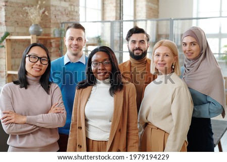Group of smiling young interracial colleagues of modern company standing together in loft open space office Royalty-Free Stock Photo #1979194229