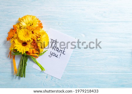 Notes thank you and coffee mug with bouquet of yellow flowers calendula on blue background. Thankfulness, coffee cup, customer service, thanks card concept, top view, flat lay. Copy space
